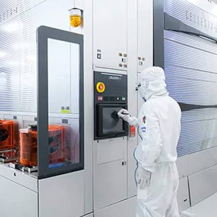 Technician operating a high-tech cleanroom control panel and automated manufacturing equipment