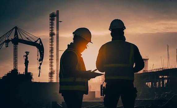 Engineers reviewing construction blueprints and site progress against a sunset silhouette